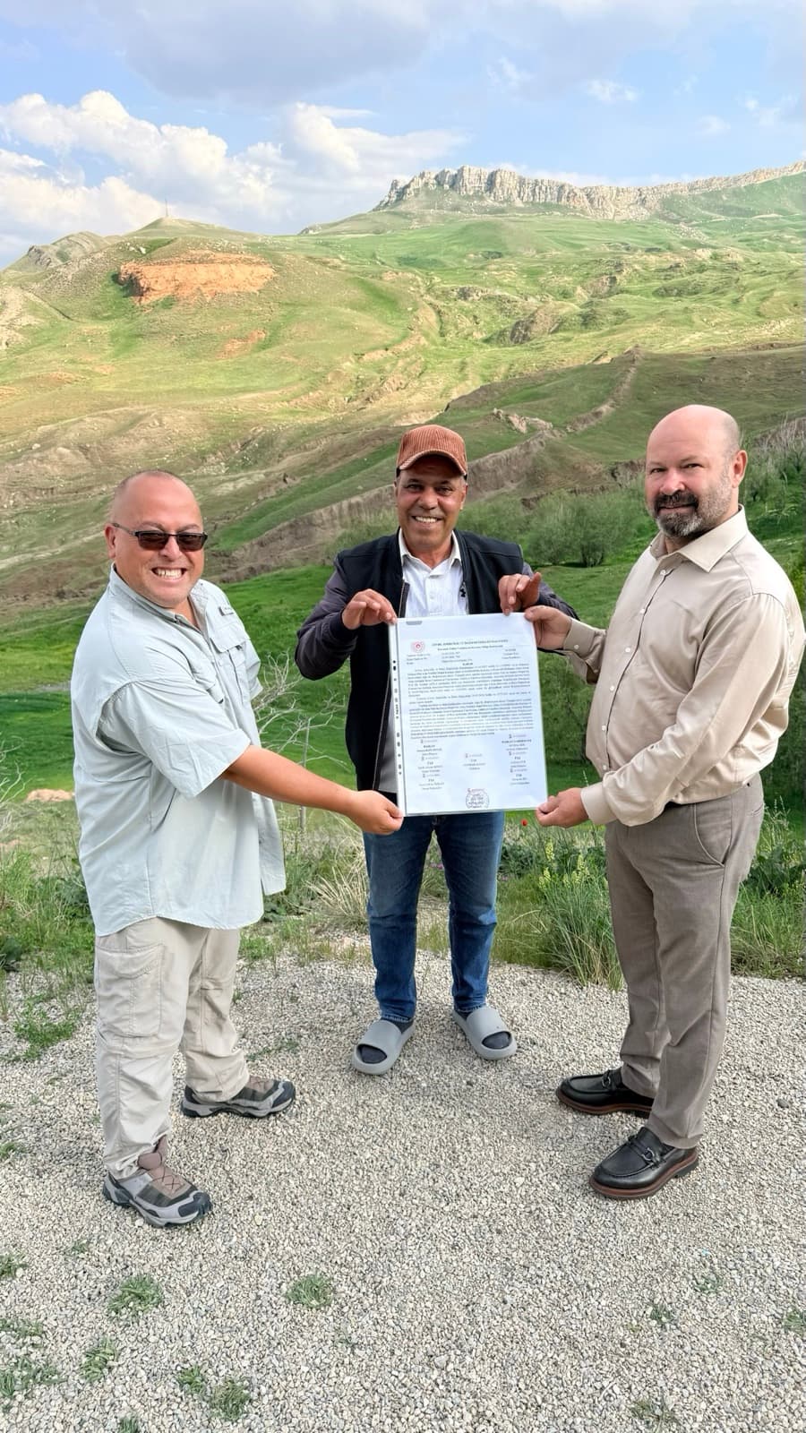 Andrew Jones and the research team holding the official authorization document at the Durupınar site, with the Mount Ararat region behind them